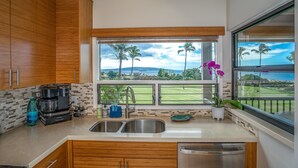 A kitchen with wooden cabinets, a coffee maker, a sink, and a view of a golf course and palm trees.