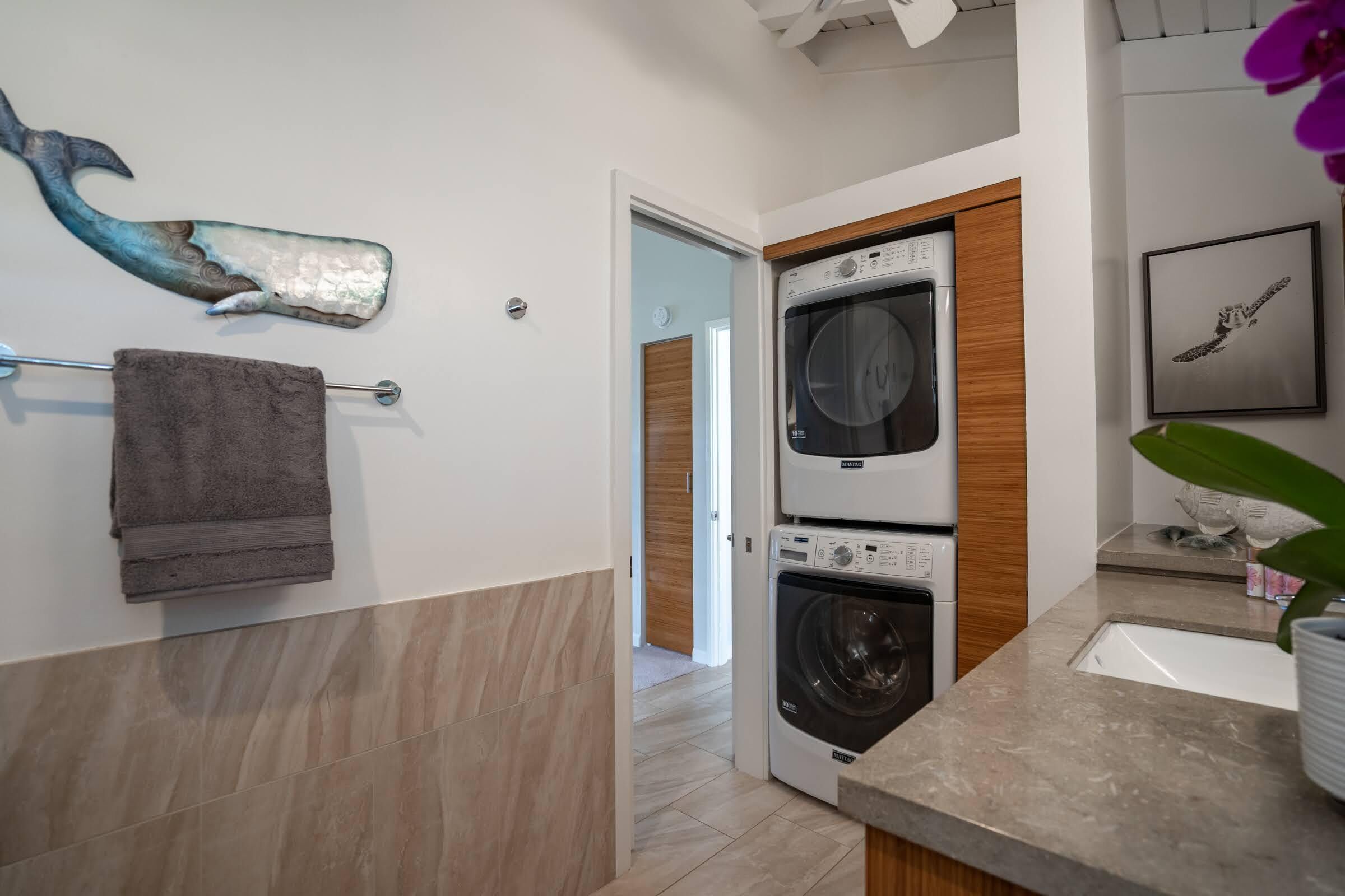 A modern kitchen with a built-in washer and dryer, a towel rack, and a decorative whale sculpture on the wall.