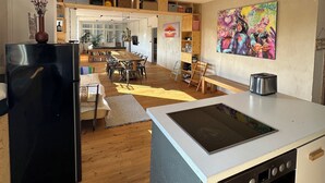 A modern kitchen with a built-in oven, a dining area with a wooden table and chairs, and a colorful artwork on the wall. - Studio Loft Filmatelier (Hamburg)