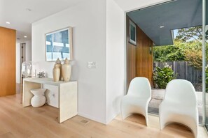 A modern interior with a white desk, two white chairs, a large window, and a painting on the wall. - Ocean View Moss Beach Retreat (Moss Beach)
