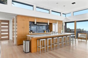 Una cocina moderna con una isla central, armarios de madera, electrodomésticos de acero inoxidable y ventanas amplias.