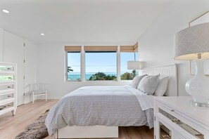 A bedroom with a large window, a bed, a nightstand, and a chair.