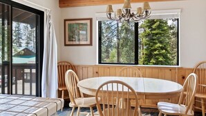 A wooden-paneled room with a round table and chairs, a chandelier, and large windows with a view of trees. - Cozy 3BDR - 1 Minute to the Beach! (Tahoe Vista)