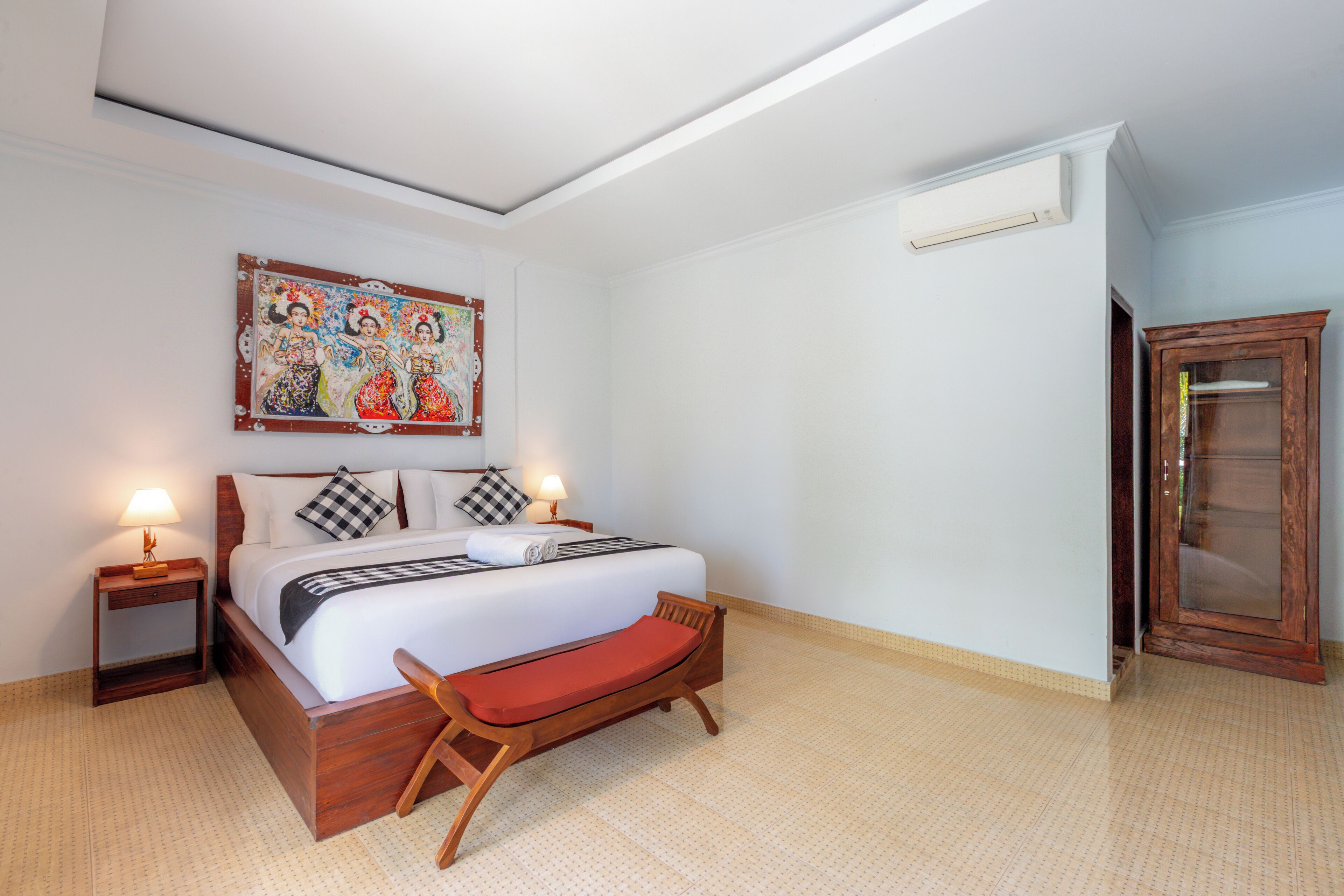 Camera d'albergo con un letto, comodini, una panca, condizionatore d'aria a parete e un armadietto in legno.