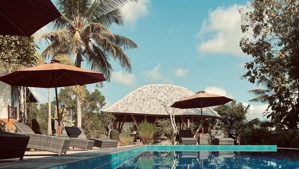 A pool area with lounge chairs and umbrellas, surrounded by palm trees and a large dome structure. - Tinggian Hill Retreat (Penida Island)