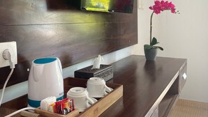 A hotel room with a wooden console table, a flat-screen TV mounted on the wall, a coffee maker, a tray with cups and condiments, and a potted orchid. - Tinggian Hill Retreat (Penida Island)