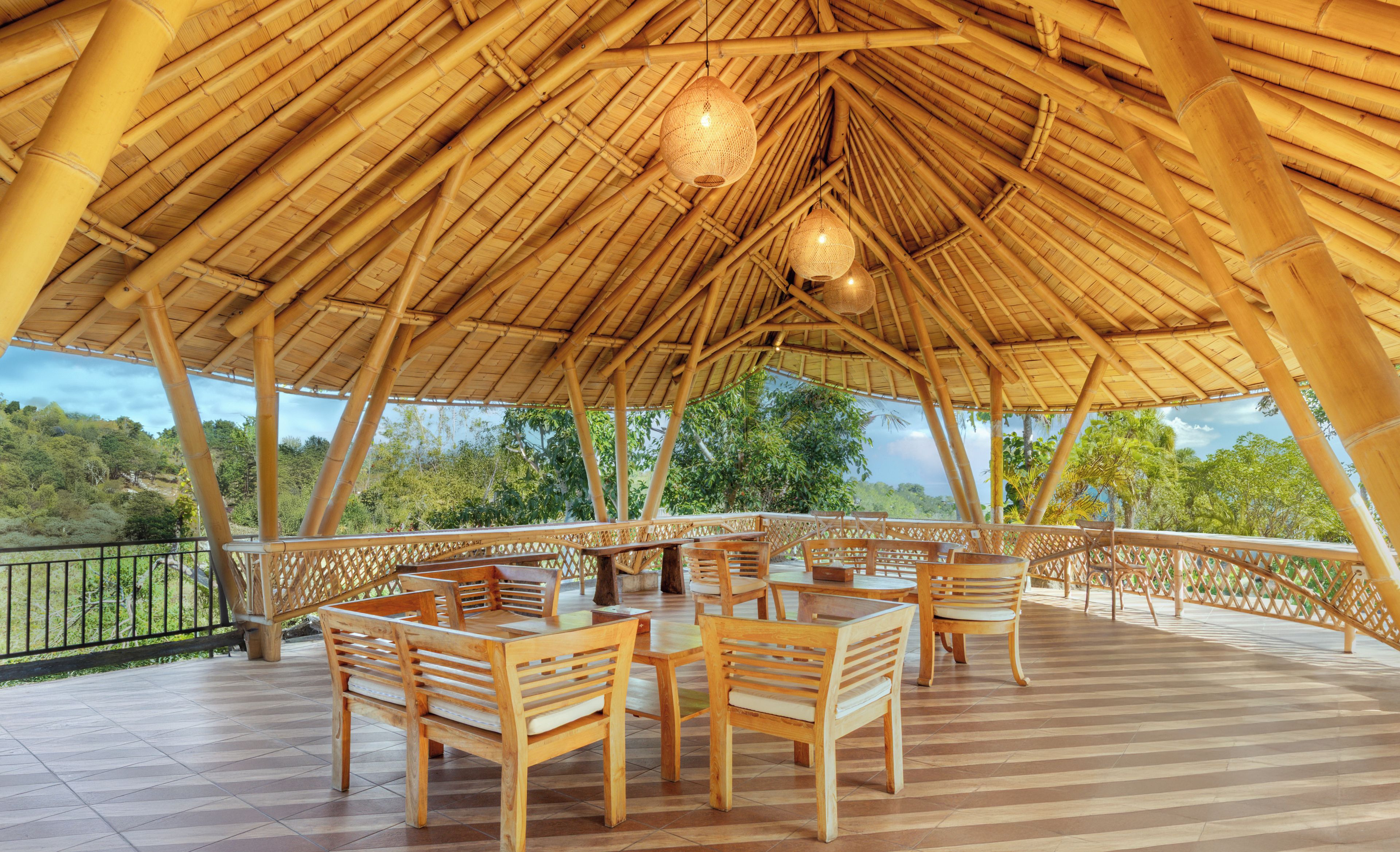 An outdoor bamboo-roofed area with wooden tables and chairs, a railing, and a view of greenery.