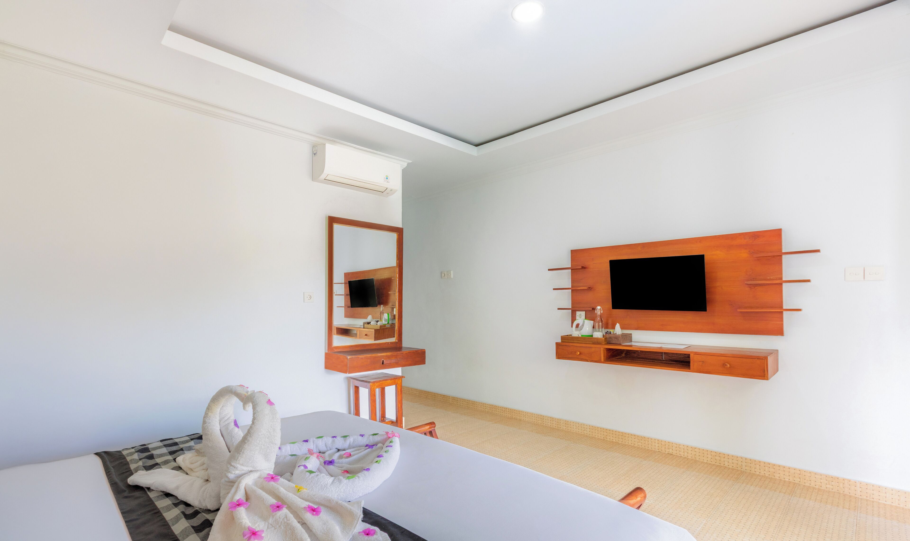 Ein Hotelzimmer mit einem Bett, einem an der Wand befestigten Fernseher, einer Holzkommode und einem Spiegel.