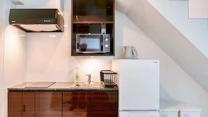 A compact kitchen with dark wooden cabinets, a microwave, a refrigerator, and a sink. - 2023 Open/Shinjuku Okubo/5 mins to JR/200M Wi-Fi (Shinjuku City)
