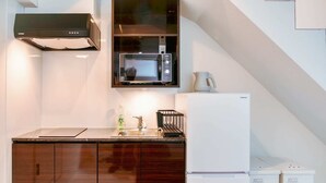 Una cucina compatta con pensili in legno scuro, un forno a microonde, un frigorifero e un lavello.