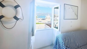 A room with a white door, a life preserver decoration, a striped sofa, a clock, and a view of a marina.