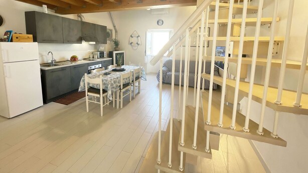 Una cocina moderna con comedor, una escalera y una sala de estar con mobiliario a rayas.