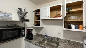 A compact kitchen with a microwave, coffee maker, and a sink. Cabinets are open, revealing storage for dishes and glassware. - Gorgeous 3Bed in the heart of South Florida (Fort Lauderdale)