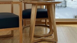 Une table à manger en bois avec deux chaises, une grande fenêtre donnant sur un paysage enneigé et un plancher en bois.