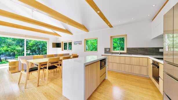 Une cuisine moderne avec des poutres en bois, un îlot central et de grandes fenêtres donnant sur un paysage verdoyant.
