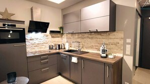 A modern kitchen with dark cabinetry, a stone backsplash, and a built-in oven. - Homely Stay -  Studio P1 (München)