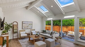 A spacious living room with a high ceiling, skylights, a sofa set, a coffee table, and a view of a wooden fence and greenery outside. - Pebble Beach's "Pebble Breeze" (Pebble Beach)