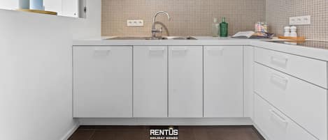 Una cocina moderna con armarios blancos, un lavamanos de acero inoxidable y un salpicadero de azulejos.