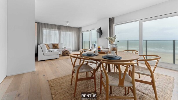 A modern living room with a dining area, large windows, and a view of the beach. - Seaflow-holiday apartment with frontal sea view (Oostduinkerke)