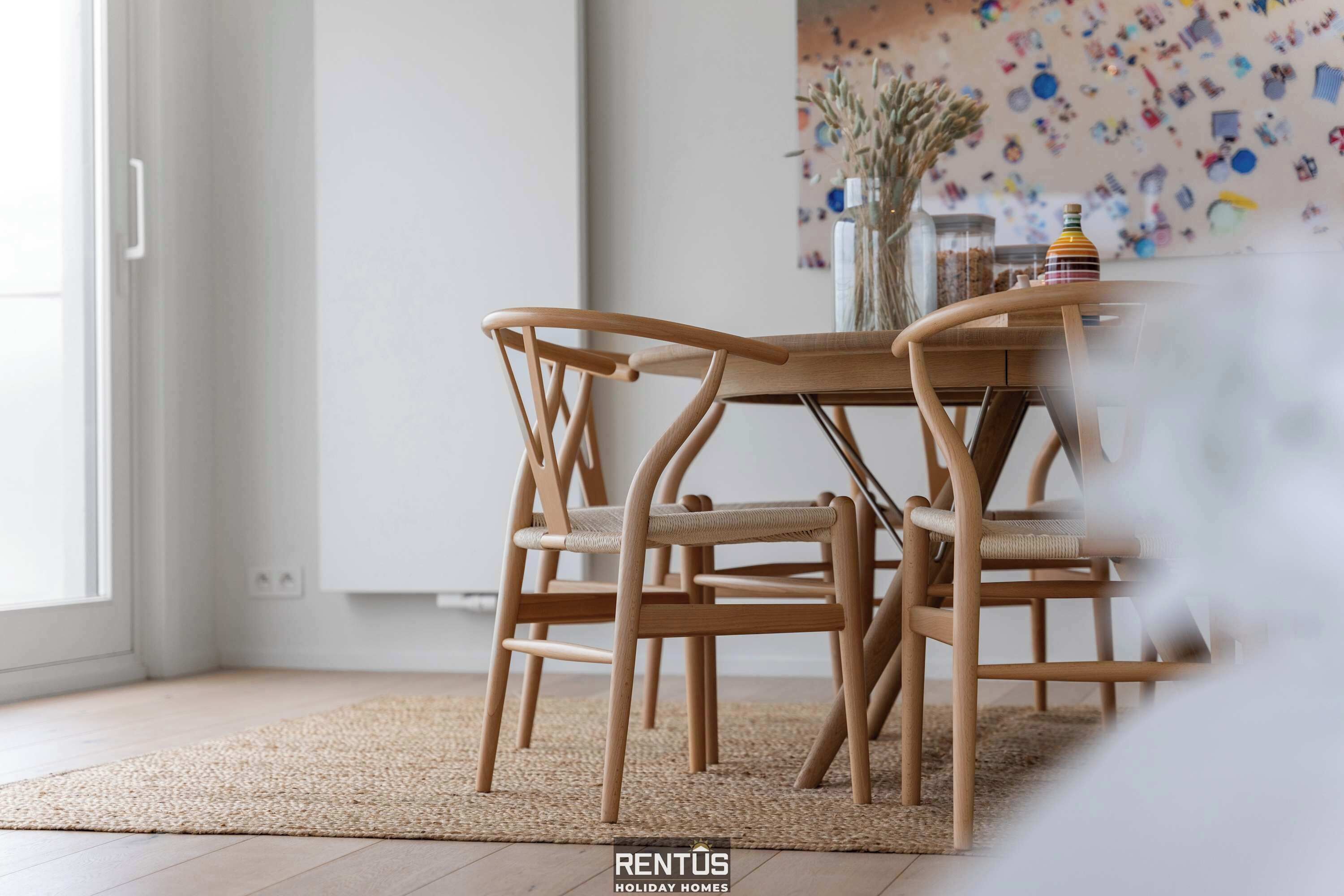 A dining area with a wooden table and chairs, a woven rug, and a decorative wall with various items.