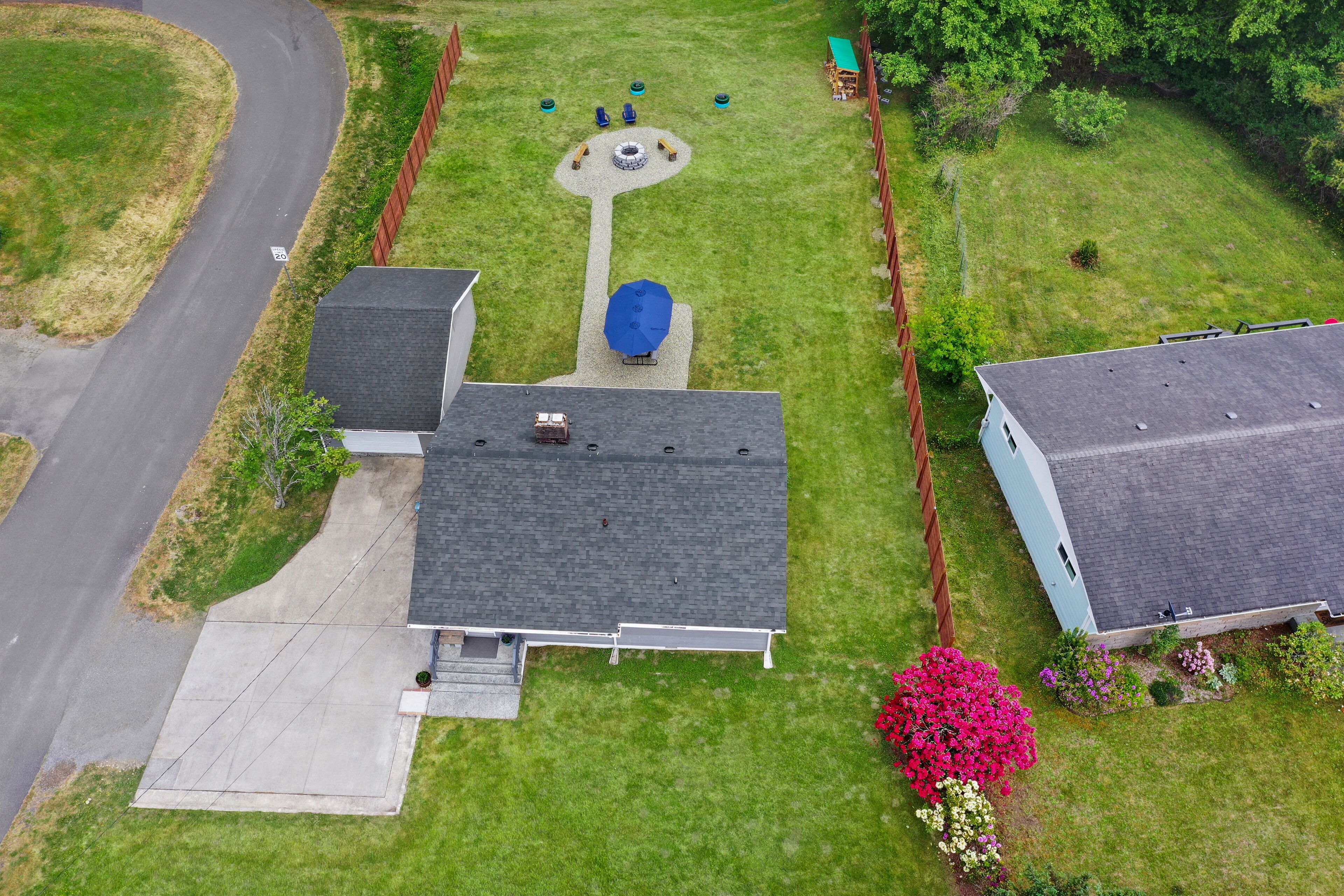 An aerial view of a residential area with a house featuring a driveway, a small patio, and a garden with a variety of plants.
