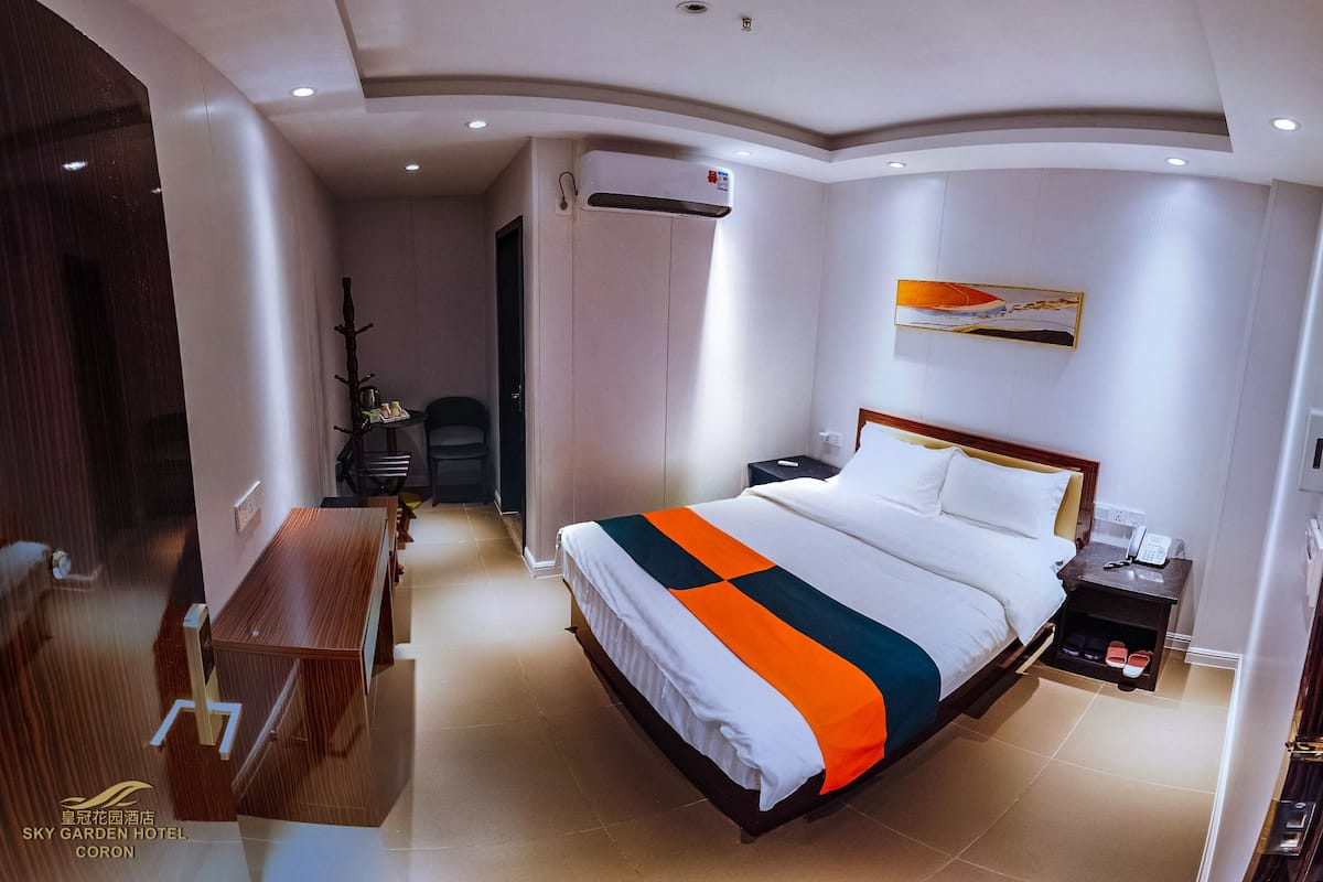 Quarto de hotel com cama, mesa de cabeceira e escrivaninha com cadeira.