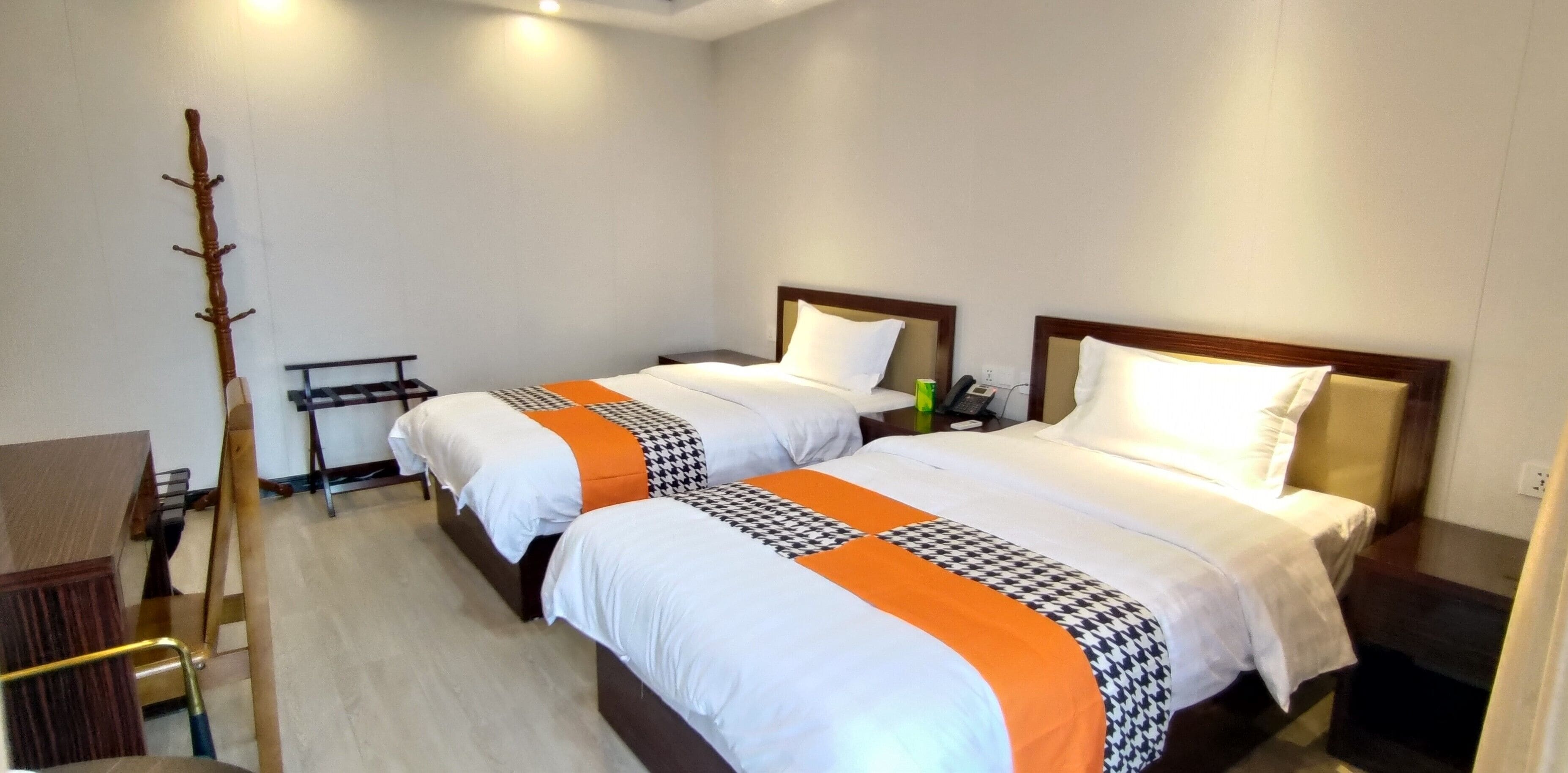 A hotel room with two beds, a wooden coat rack, a small table, and a chair.