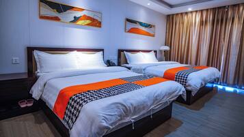 Een hotelkamer met twee bedden, elk voorzien van witte beddengoed en oranje accenten, een plafondlamp en een groot raam met gordijnen.