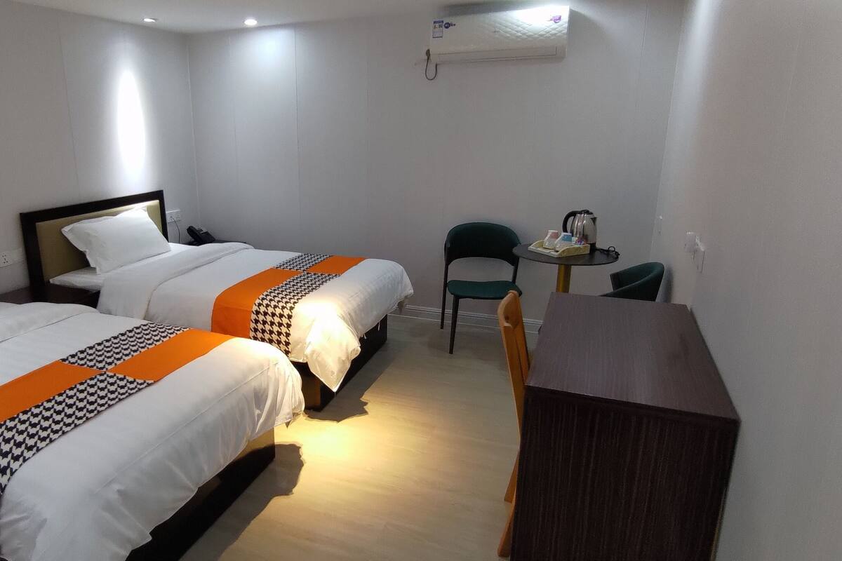 Quarto de hotel com duas camas, uma escrivaninha, uma cadeira e uma mesinha.