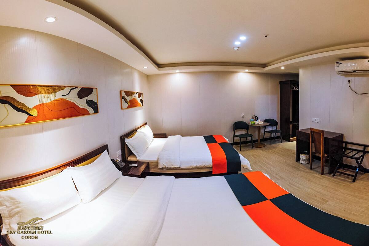 Quarto de hotel com duas camas, uma escrivaninha, cadeiras e obras de arte nas paredes.