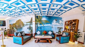 A hotel lobby with a tropical mural, blue sofas, a wooden coffee table, and a bookshelf. - Sky Garden Hotel (Coron)