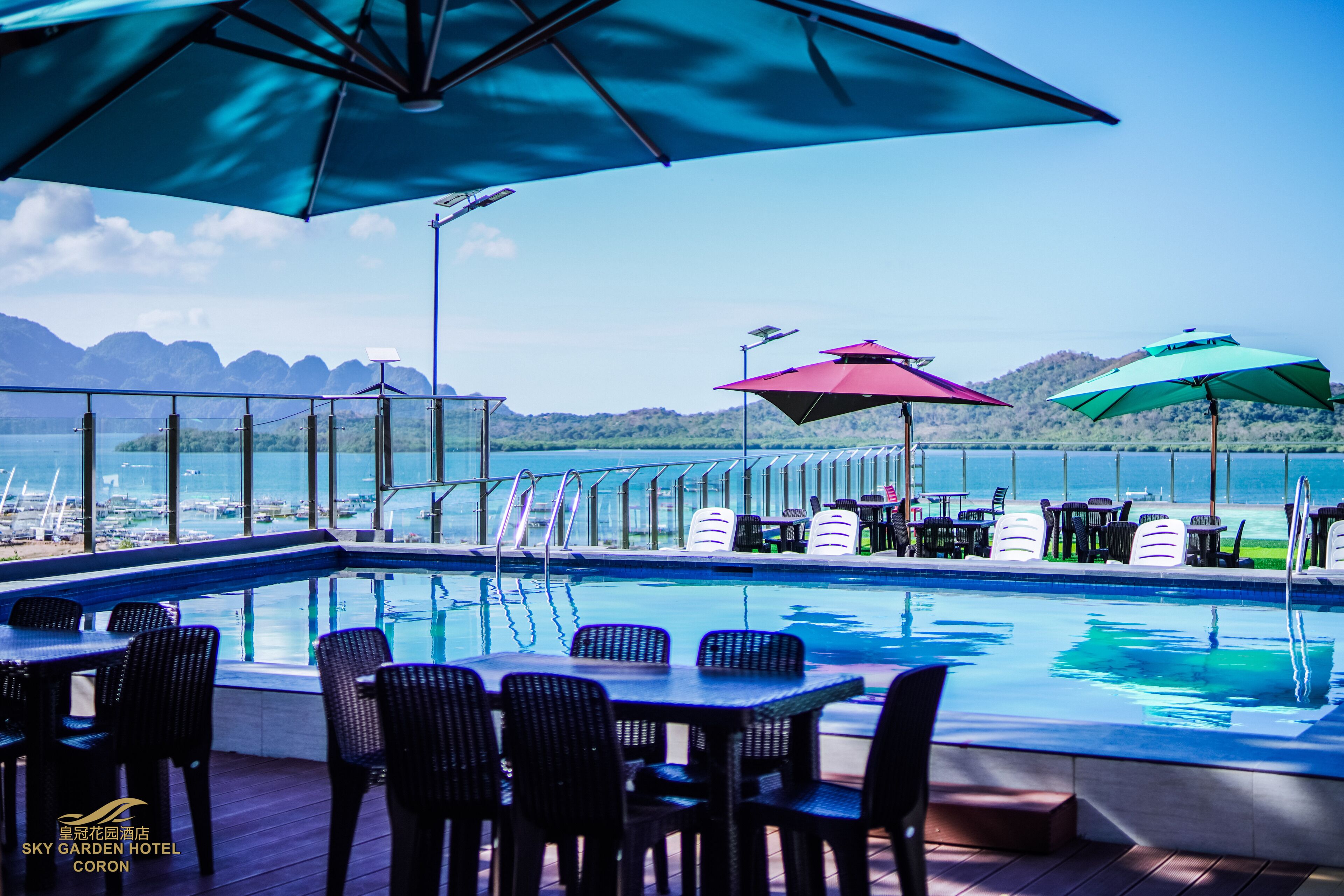 A poolside area with a view of the water, lounge chairs, and umbrellas.