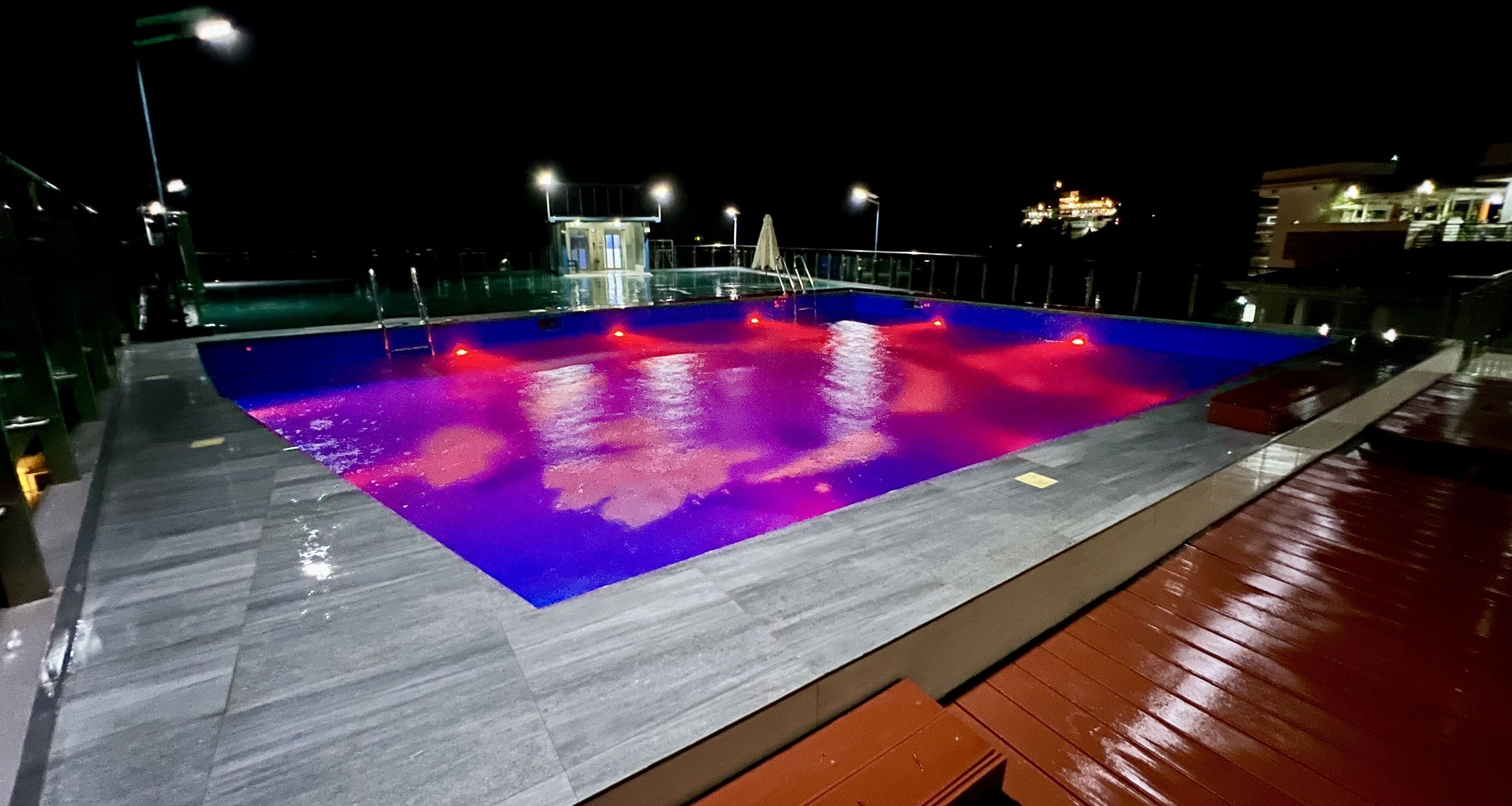 A swimming pool with a blue and red illuminated deck at night.