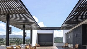 A rooftop terrace with wooden flooring, a seating area with chairs, and a view of the landscape.