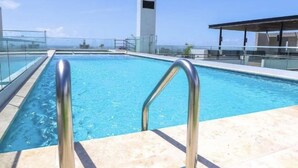 A swimming pool with metal railings, a clear blue sky, and a distant view of a building.