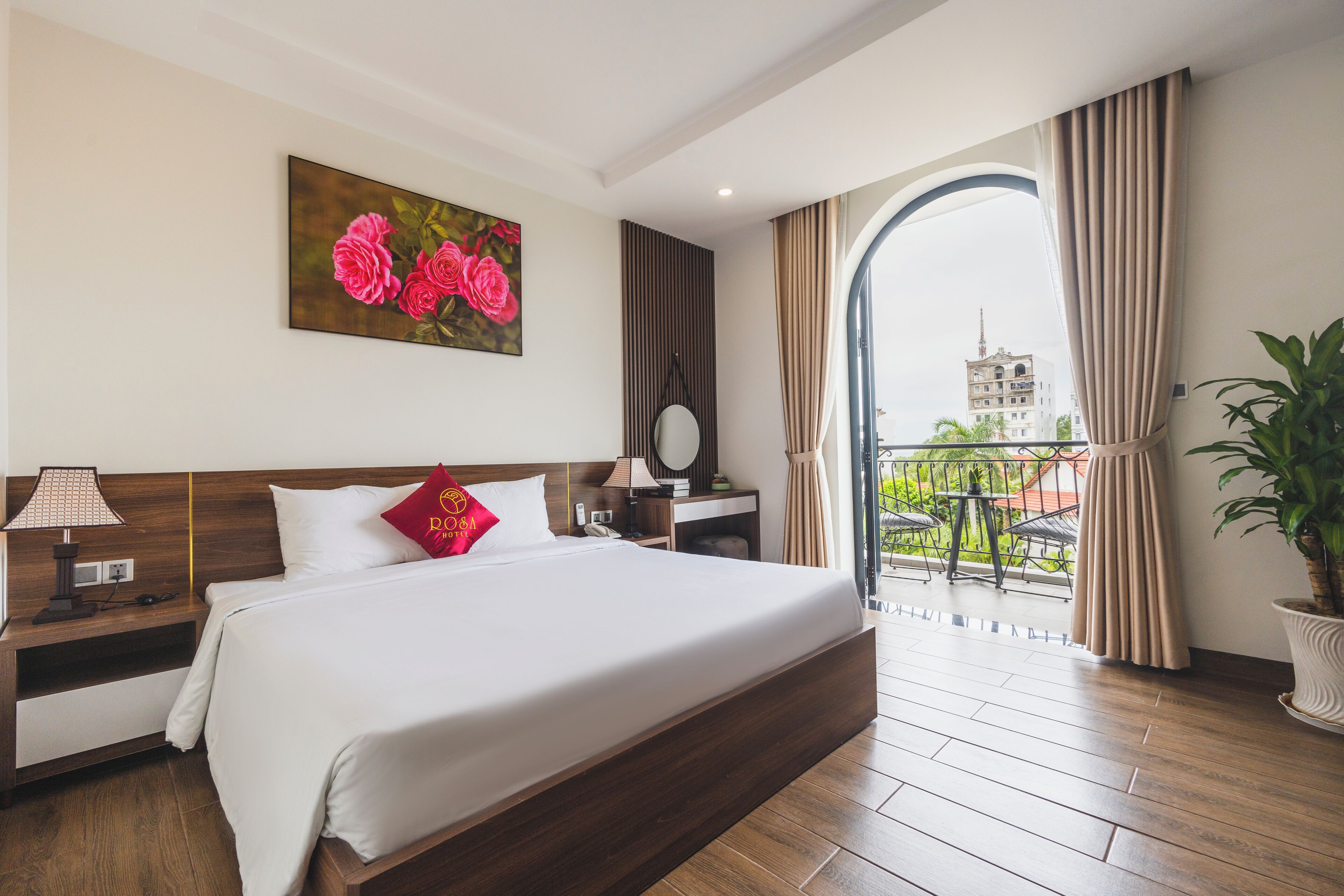 Ein Hotelzimmer mit einem großen Bett, einem Nachttisch, einem Spiegel, einem Fenster mit Vorhängen und Blick auf ein Gebäude.