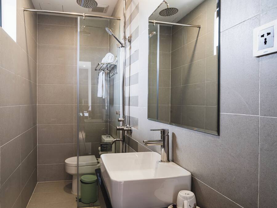 Un baño moderno con ducha envuelta en vidrio, lavamanos blanco y retrete.