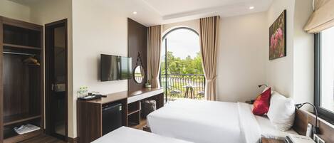 A hotel room with two beds, a desk with a TV, a wardrobe, and a balcony with a view.