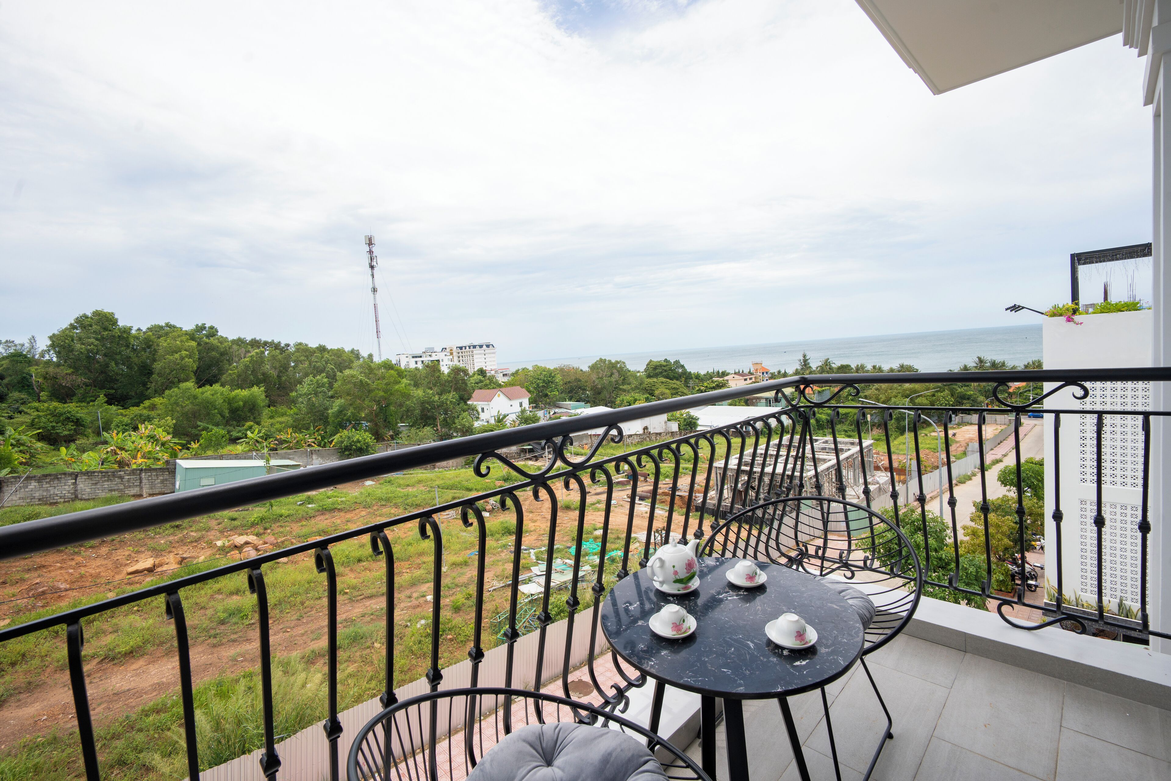 A balcony with a table and chairs, overlooking a view of the sea and greenery.