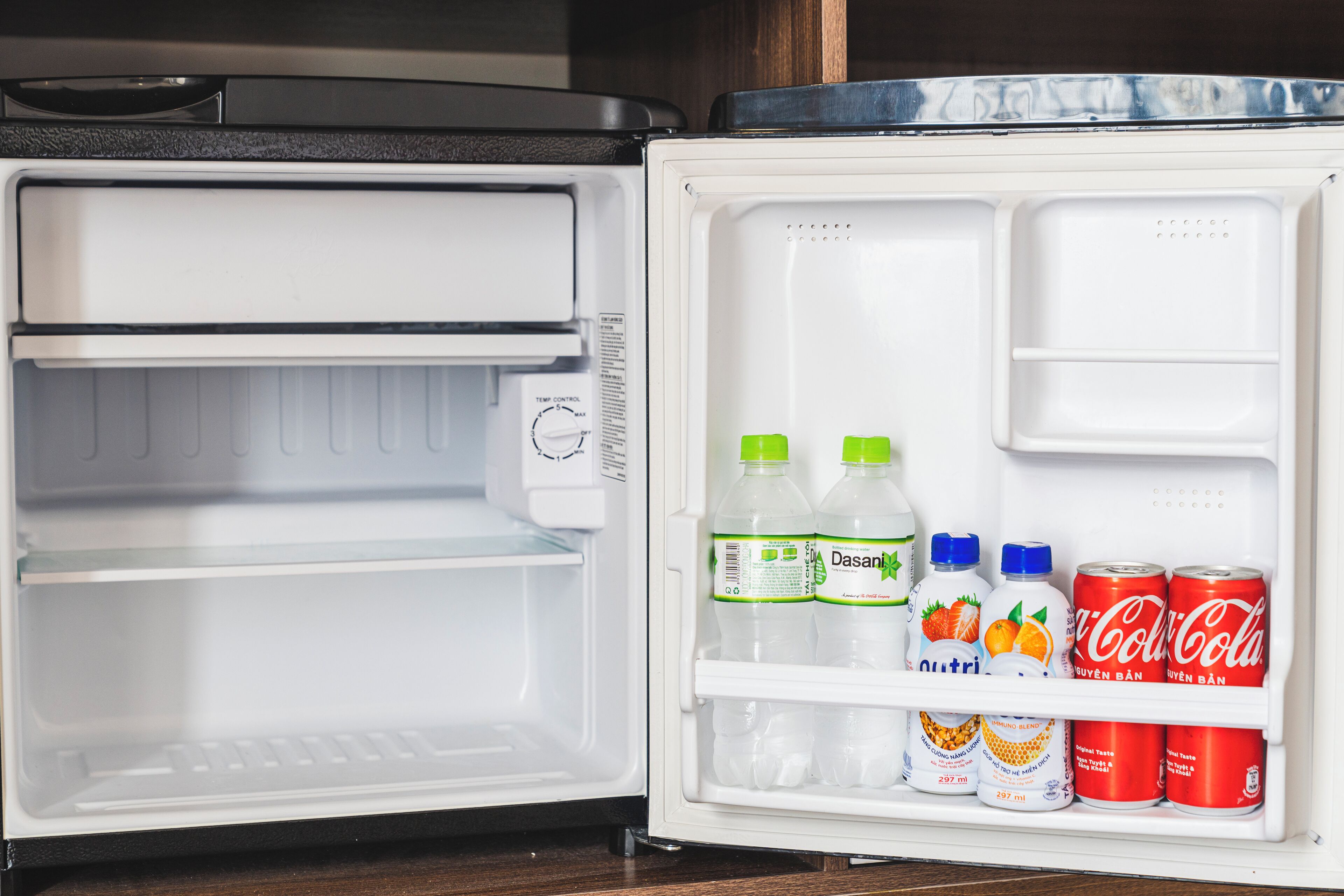 An open refrigerator with shelves containing Dasani water bottles, Outri orange juice, and Coca-Cola cans.