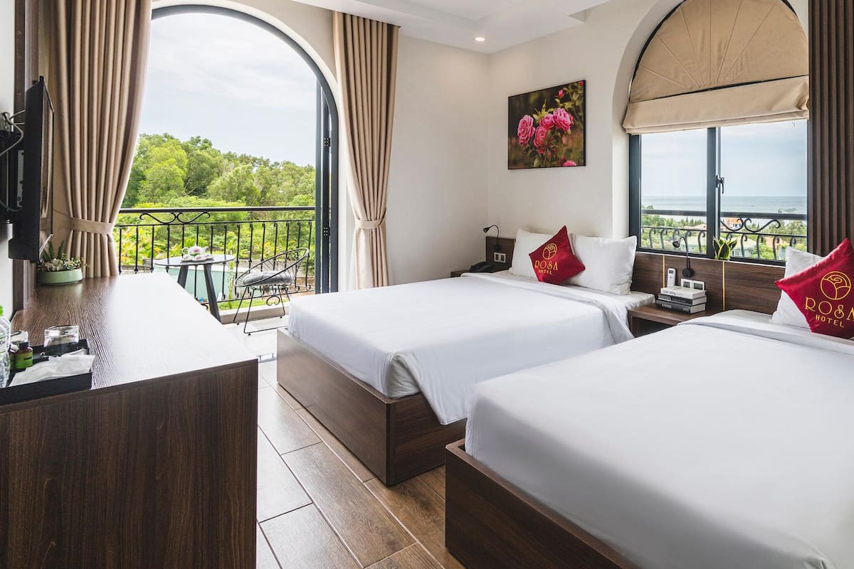 A hotel room with two beds, a balcony with a view, a desk with a phone, and a TV mounted on the wall.