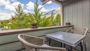 A balcony with a table and chairs, overlooking a mountainous landscape with trees and houses. - Top Floor Mountain View with Pool & Hot tubs (Canmore)
