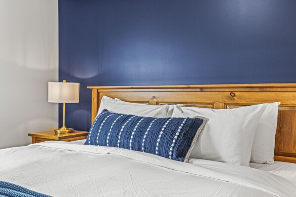 A bed with white bedding, a blue and white patterned pillow, and a wooden headboard. - Top Floor Mountain View with Pool & Hot tubs (Canmore)