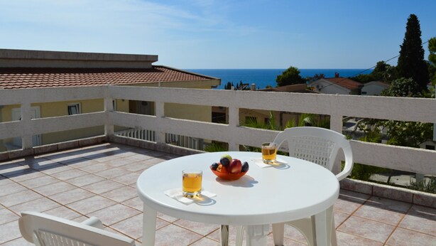 A round white table with two chairs, a bowl of fruit, and two glasses of beer on a tiled patio overlooking a coastal view. - The only apartment in a detached house (Bar)