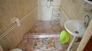 A bathroom with a toilet, sink, shower, and a small step with a mat. - The only apartment in a detached house (Bar)