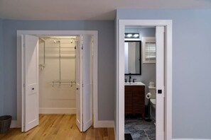 A room with a wooden floor, a walk-in closet with shelves, a bathroom with a sink and toilet, and a mirror on the wall. - Lake Access 4 Bed 3 Full Bath (Billerica)