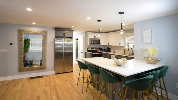 Una cocina moderna con una isla central, electrodomésticos de acero inoxidable y taburetes de bar verdes.