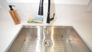 Un lavamanos de acero inoxidable con un grifo moderno, un dispensador de jabón y un cepillo para lavar platos.