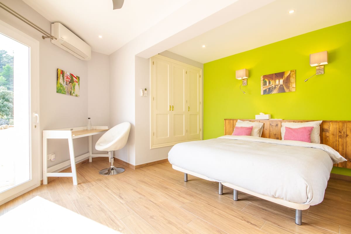 Une chambre à coucher avec un lit, un bureau et une chaise. Il y a une fenêtre, une porte et un mur décoré de tableaux.