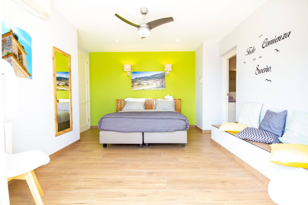 Une chambre lumineuse avec un lit, un canapé et un ventilateur de plafond.